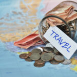 Jar of cash and coins tipped over on a world map with a label that says "travel"