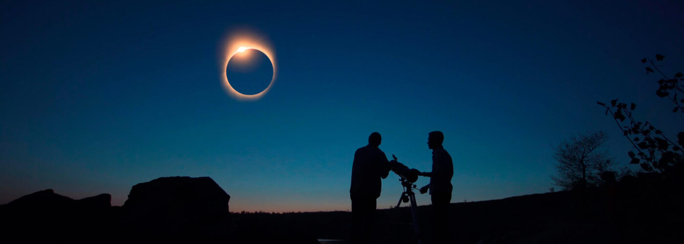 Silhouettes of people watching an eclipse through a telescope