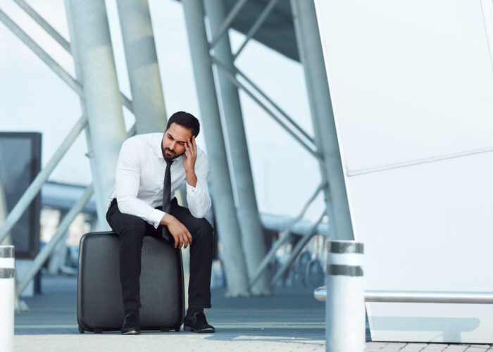 Distressed man sitting on his rolling suitcase at airport