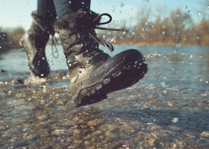 Close up of someone wearing fuzzy waterproof boots, splashing through a puddle on a cobblestone surface