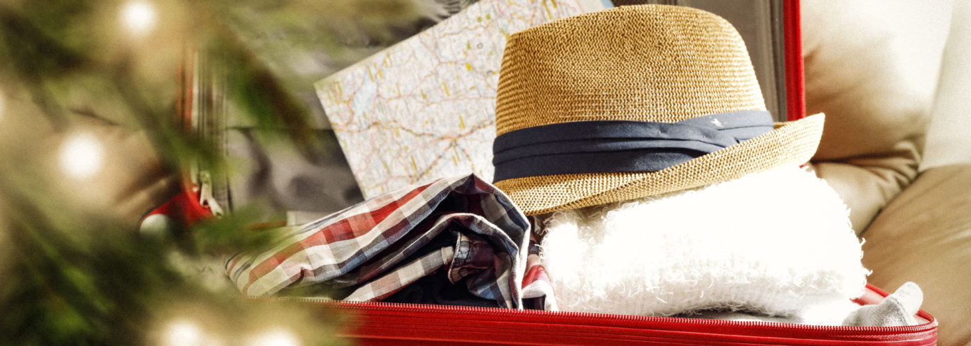 Suitcase packed with travel gear in background with blurry Christmas tree in foreground