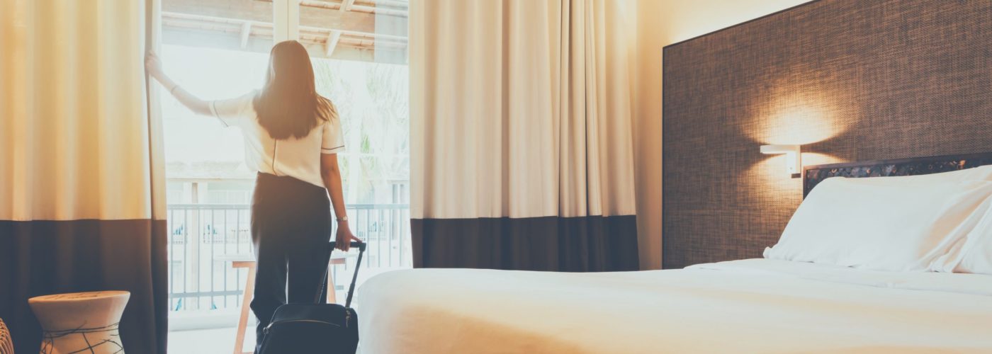 Woman pulling a rolling suitcase, looking out the window of her hotel room