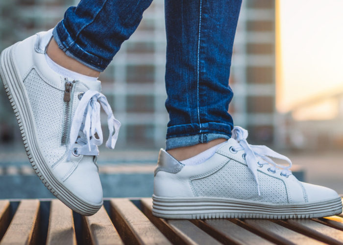 Woman wearing white sneakers walking in city at sunset