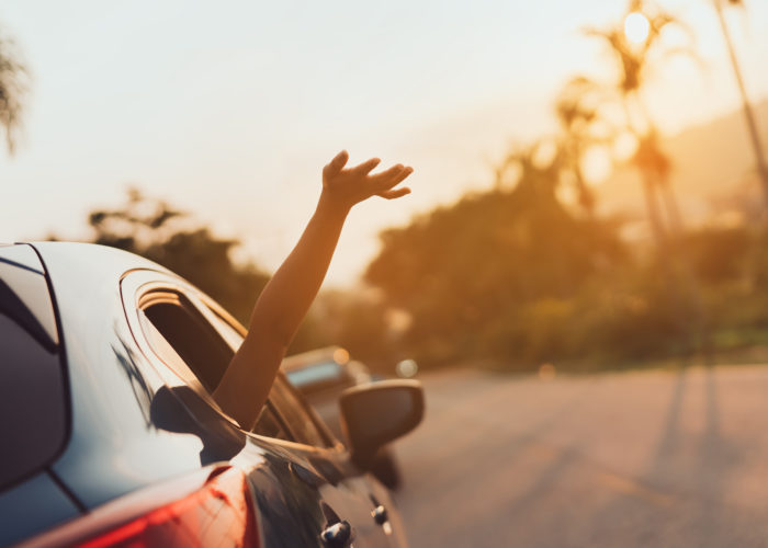 Person sticking hand out of window of car as car drives down street at sunset