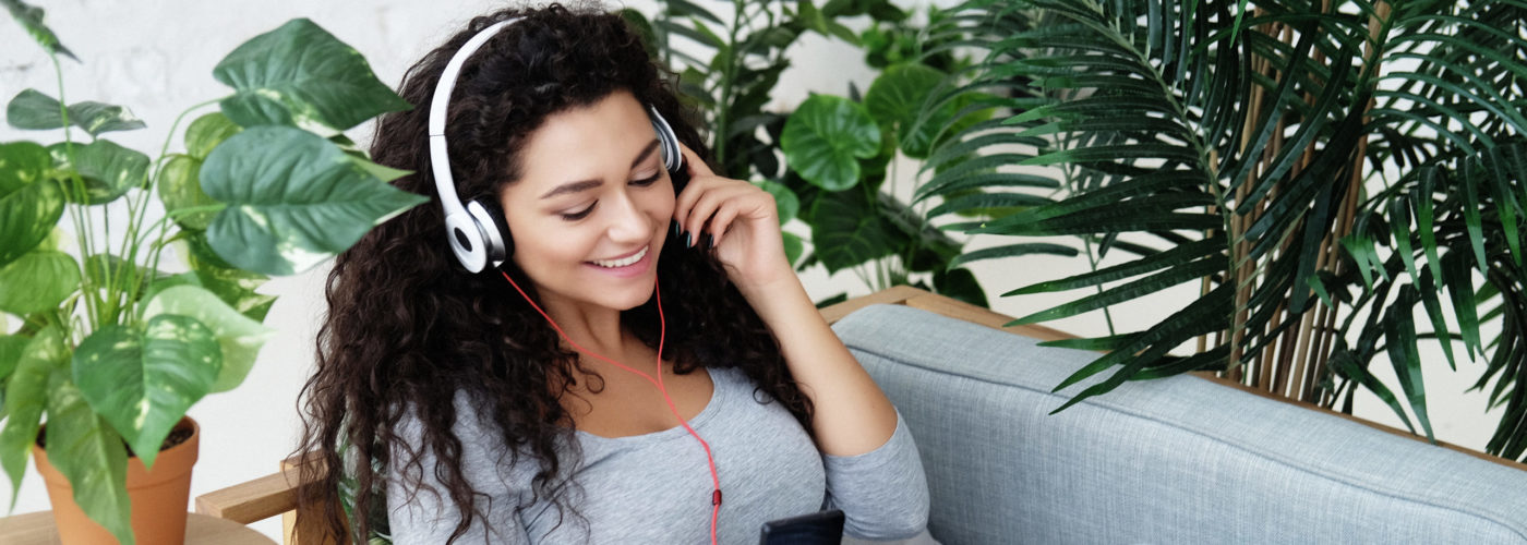 Women sitting amongst houseplants on a sofa listening to music on her phone