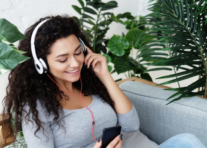 Women sitting amongst houseplants on a sofa listening to music on her phone