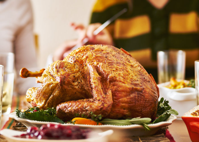 Family enjoying Thanksgiving dinner out of focus in the background with turkey in focus in the foreground