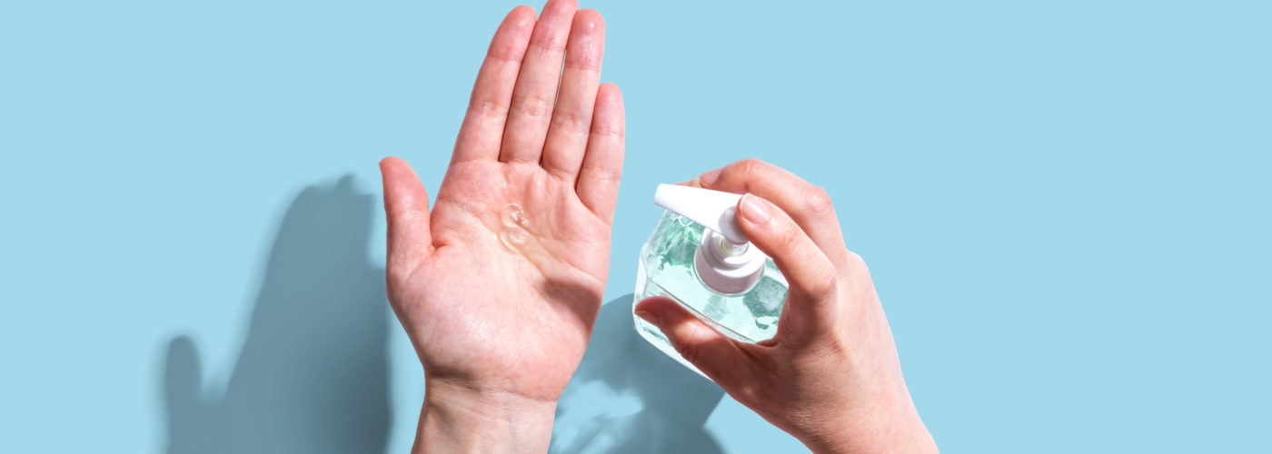 Bird's eye view of person sanitizing their hands on a light blue backdrop