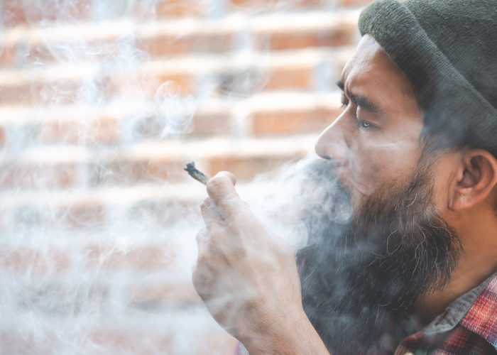 Man smoking a marijuana joint in front of a brick wall