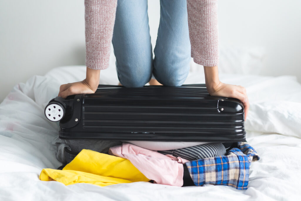 Close up of person kneeling on overflowing suitcase to get it to close