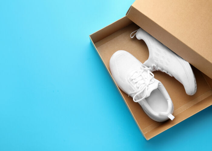 New white shoes inside brown shoe box on a bright blue background