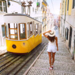 Woman wearing summer clothes, walking down a street in Lisbon, Portugal past a tram