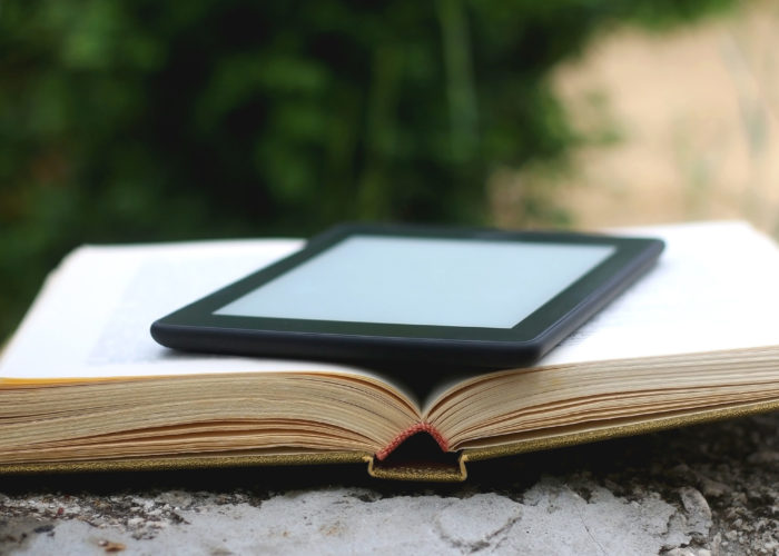 eReader laying on top of an open paper book outside on a cement ledge