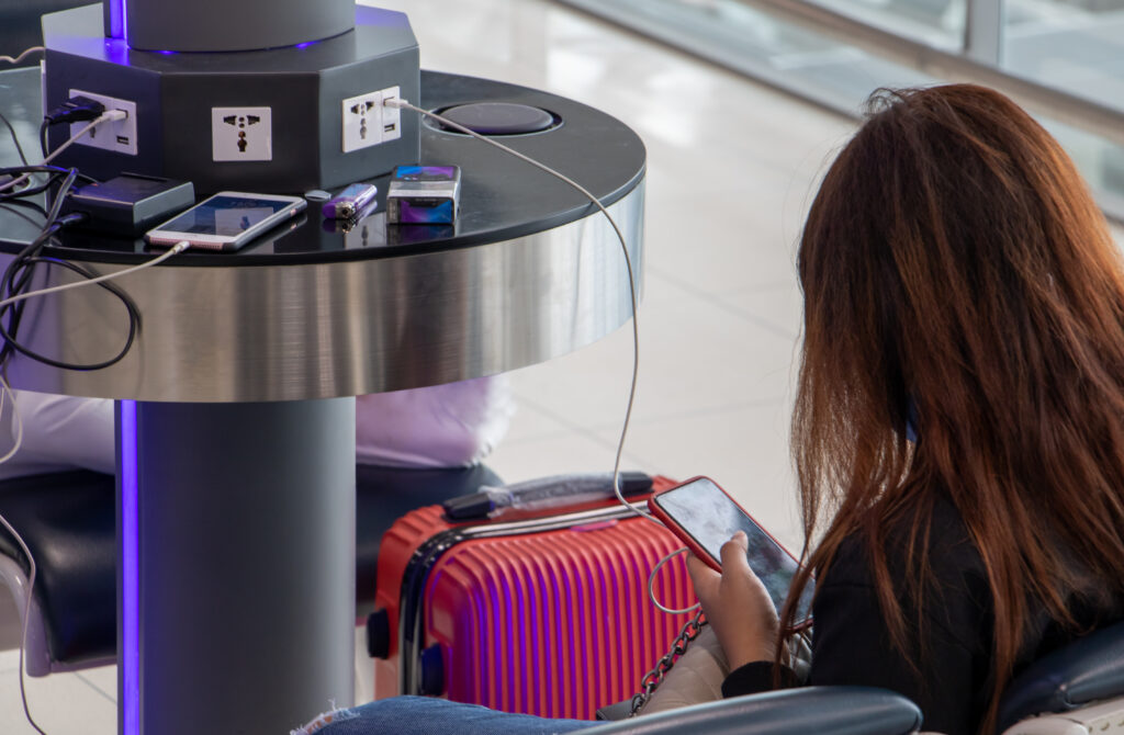 Woman sitting at airport charging station with phone plugged in