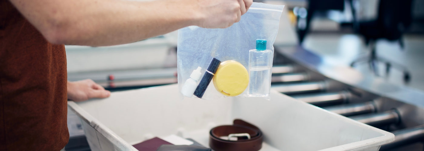 Person removing clear bag of liquid bottles from carry on luggage and placing them in security bin