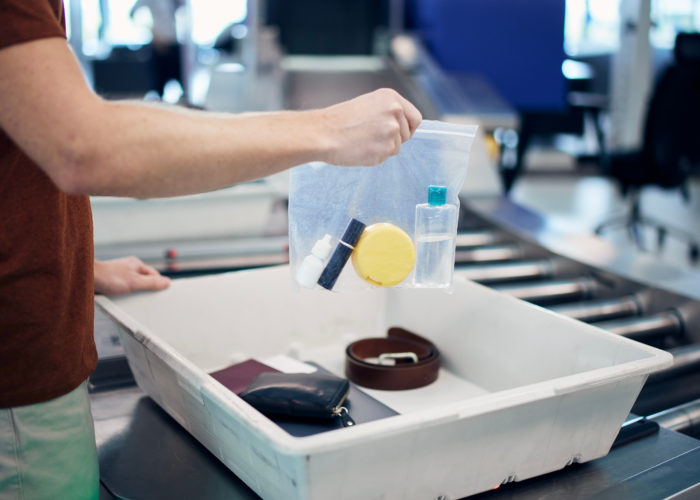 Person removing clear bag of liquid bottles from carry on luggage and placing them in security bin