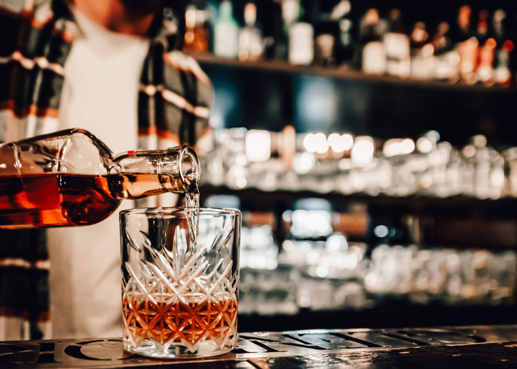 Close up of bartender pouring a drink at a fully stocked bar