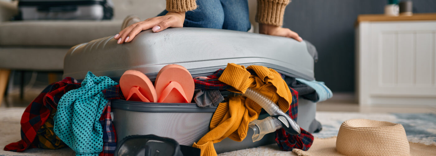 Close up of person pressing down top of overfull suitcase