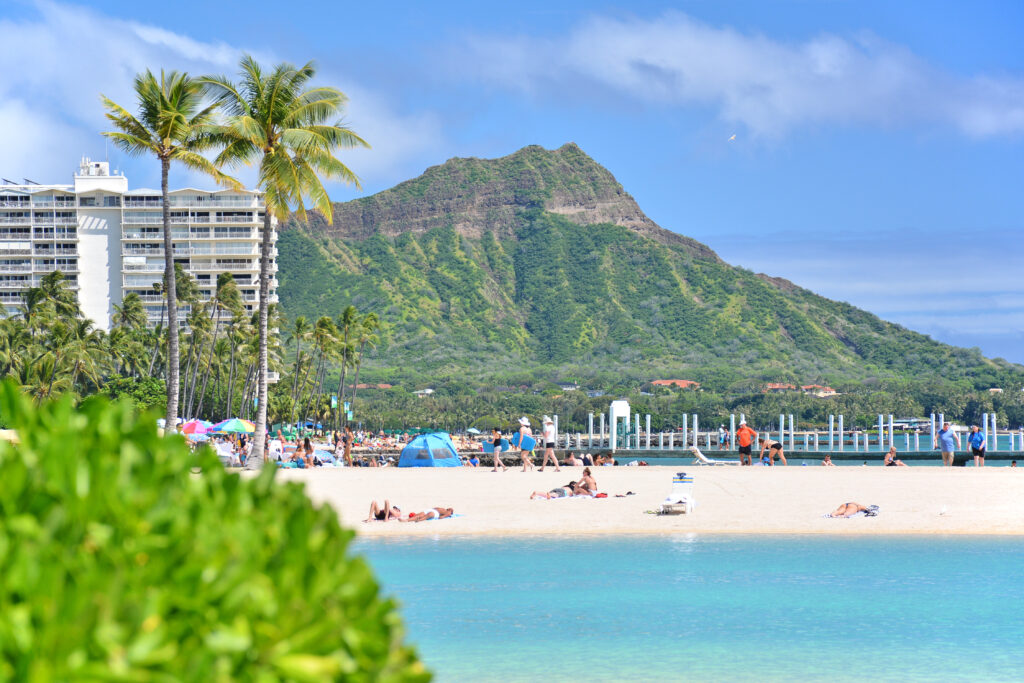 View from across the ocean looking at a white sand beach with hotel and mountain in background