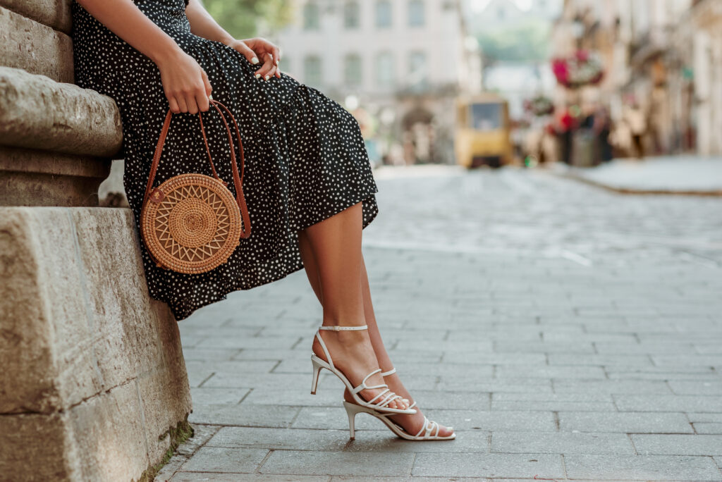 Close up of person wearing dress and low heels resting on a stone wall in a European city