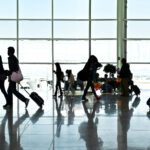 Silhouettes of people walking past a large window in an airport terminal