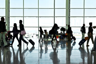 Silhouettes of people walking past a large window in an airport terminal