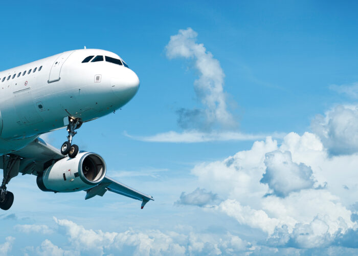 Airplane mid-flight in a blue sky with white clouds