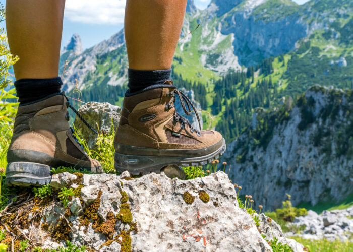 Close up of person from the knees down, wearing hiking boots and standing on a cliff overlooking a green mountainous landscape