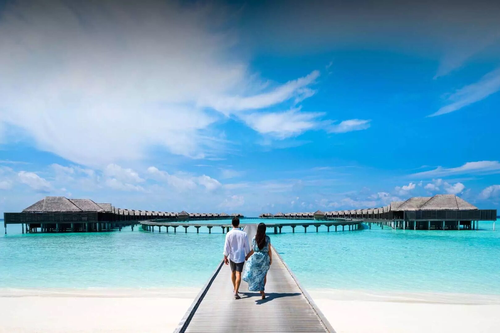 Couple walking towards circle of overwater bungalows at Anantara Kihavah Villas, Kihavah on Huravalhi Island in the Maldives