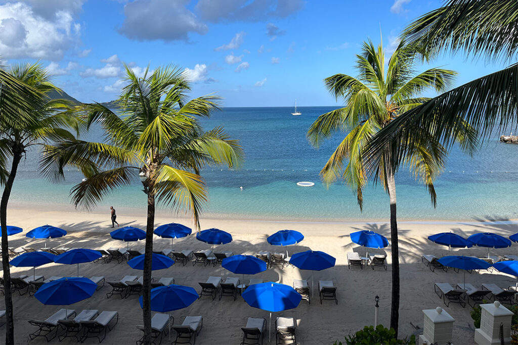 Lounge chairs on the beach surrounded by palm trees as seen from a suite deck at The Landings Resort & Spa in Saint Lucia