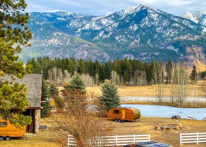 Two cabins and two small wooden trailers surrounded by trees on a backdrop of tall mountains at ROAM Beyond