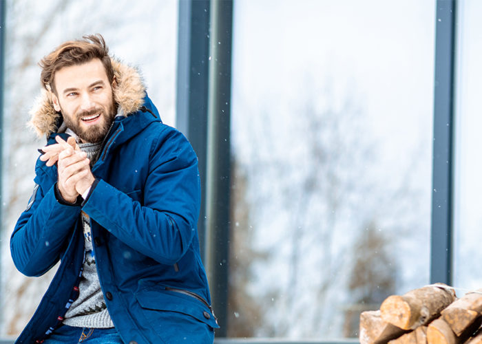 Man sitting on porch during a light snow next to a pile of chopped wood