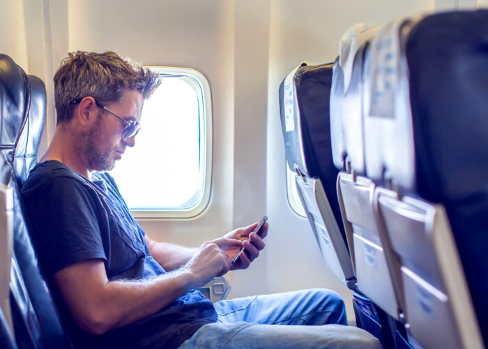 Man with dark hair is reading text message on mobile phone in airplane seat