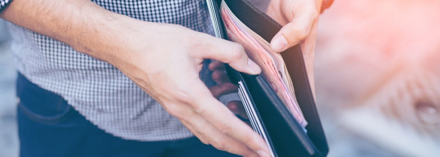 Man standing holding black wallet full of money.